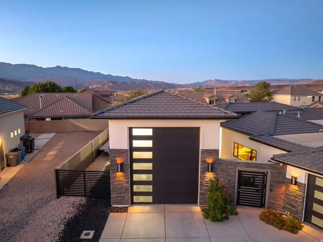 Modern exterior featuring a dark garage door with horizontal glass panels, stone veneer accents, and an architectural metal gate