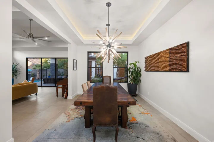 Recessed tray ceiling with integrated lighting, modern chandelier, dark-framed windows, and tile flooring