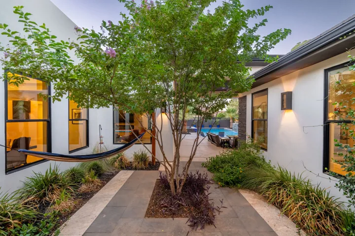 Patio area featuring a paved walkway, mature tree, established landscaping, exterior lighting, and large windows