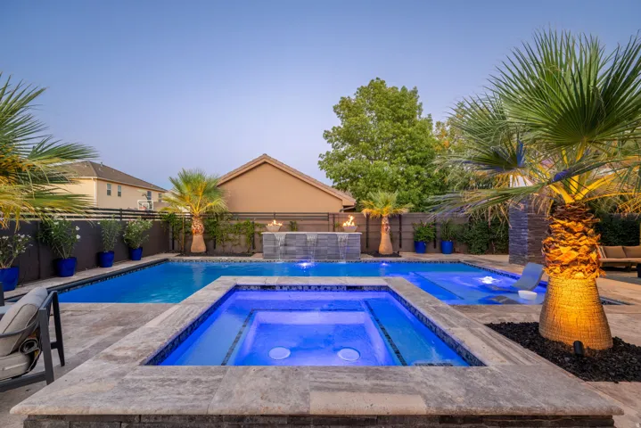 Backyard oasis featuring a swimming pool, integrated spa, stone fire feature, and mature palm trees