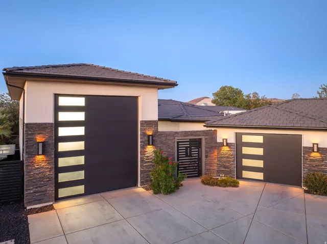 Modern façade featuring a segmented concrete driveway, stacked stone accents, contemporary garage doors with frosted glass panels, and exterior sconce lighting