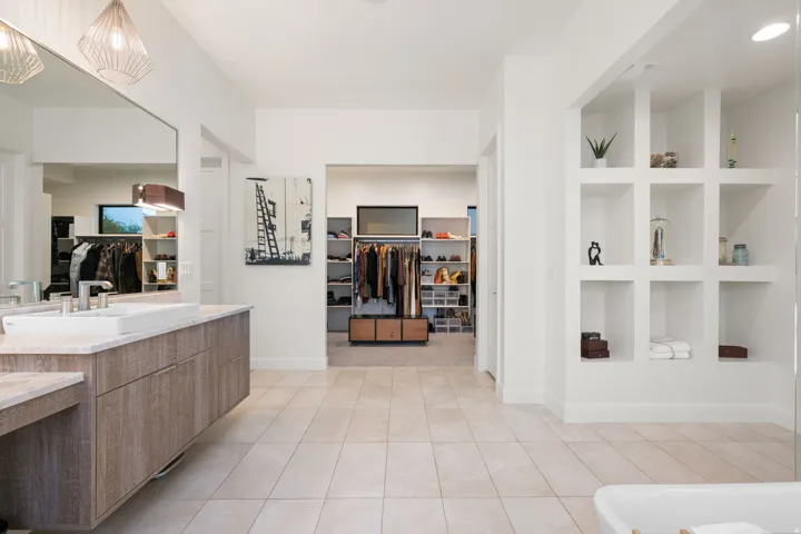 Floating wood-finish vanity with an undermount sink, large wall-mounted mirror, recessed lighting, and built-in shelving