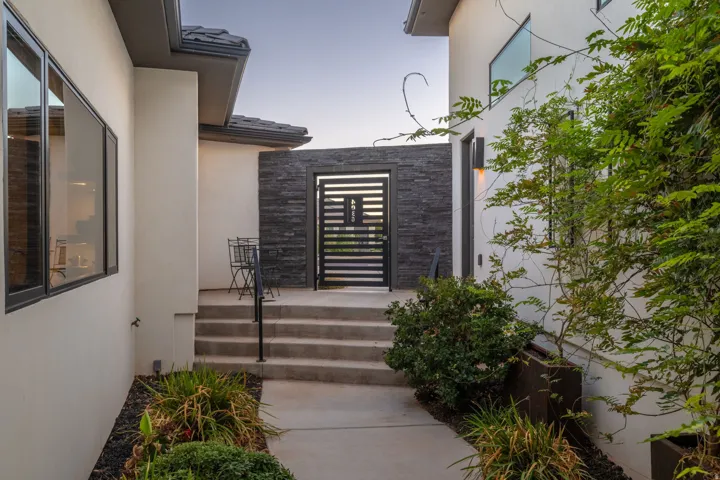 Exterior entrance featuring a decorative gate, stone accent wall, concrete steps, and integrated landscaping