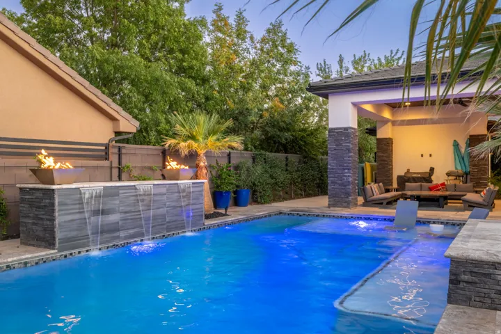 Swimming pool with integrated water features, stone-clad fire bowls, a covered patio with stacked stone columns, and surrounding hardscaping