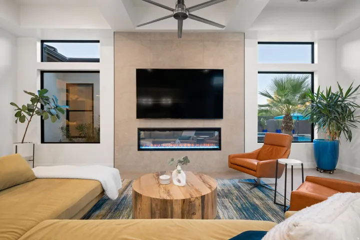 Recessed ceiling with a modern ceiling fan, large format tile fireplace surround, linear electric fireplace, and multiple black-framed windows