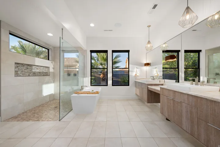 Spacious bathroom featuring a freestanding tub, expansive tiled shower with a pebble floor, dual vanities with under-mount sinks, and large format floor tiling