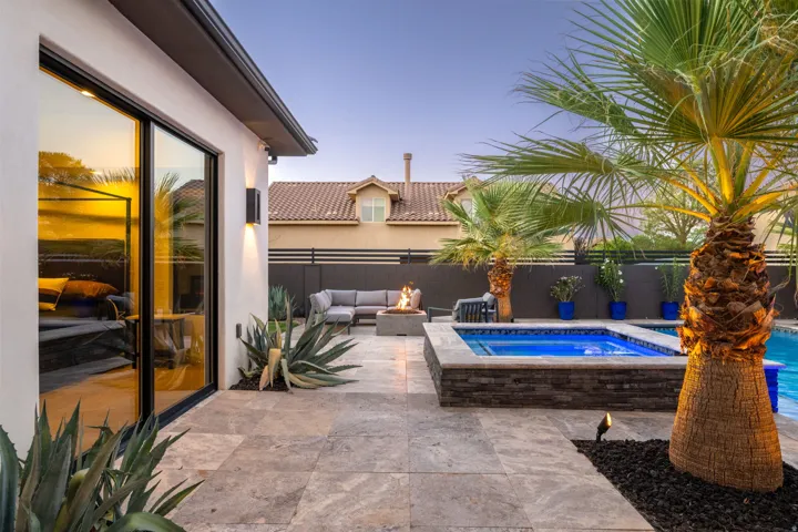 Outdoor living area featuring a built-in spa, travertine paver patio, and mature palm trees