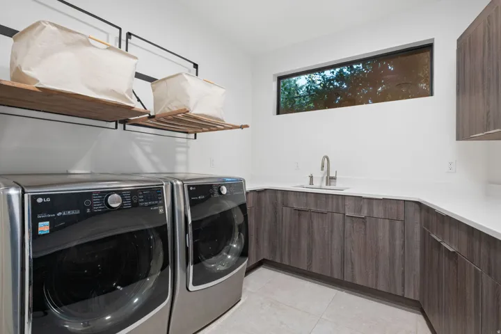 Laundry room featuring wood-finish cabinetry, white countertop, stainless steel sink with a gooseneck faucet, and a horizontally oriented window