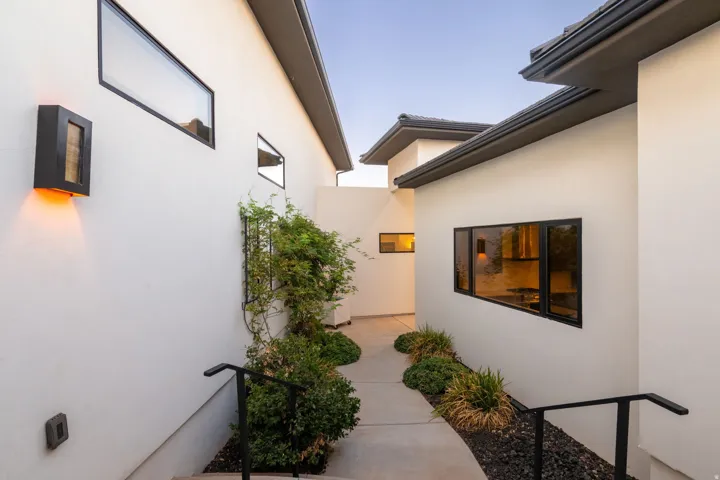 Modern exterior featuring white stucco, black-framed windows, contemporary outdoor lighting, and integrated landscaping with dark decorative rock