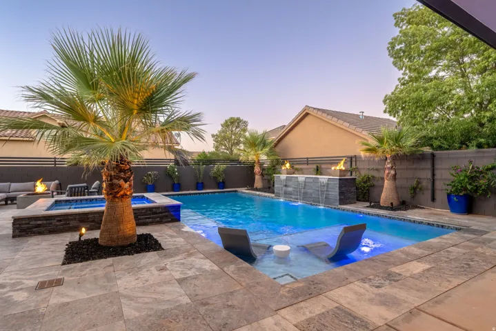 Resort-style backyard featuring a swimming pool, integrated spa, stone paver patio, fire pit, and a water feature with fire bowls