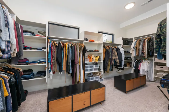 Spacious walk-in closet featuring extensive built-in shelving, multiple hanging rods, and two built-in storage benches