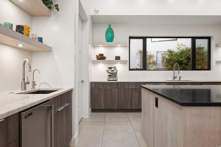 Contemporary kitchen featuring wood-finish cabinetry, light-toned countertops, a black island countertop, and floating shelves with integrated lighting