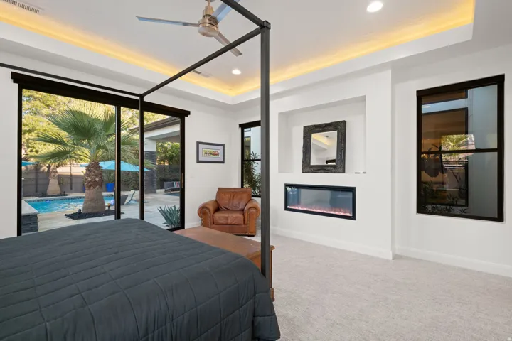 Recessed electric fireplace, tray ceiling with cove lighting, ceiling fan, and large sliding glass doors opening to a pool