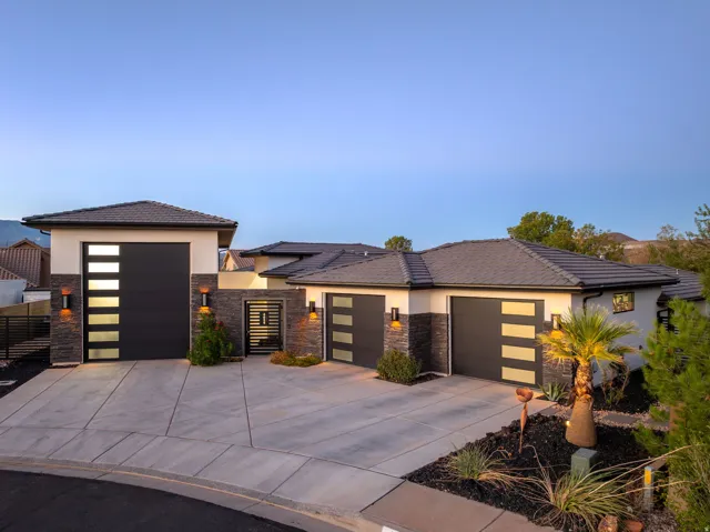 Modern architectural design featuring stacked stone accents, multiple garages with contemporary doors, a private courtyard entry, and a tiled roof