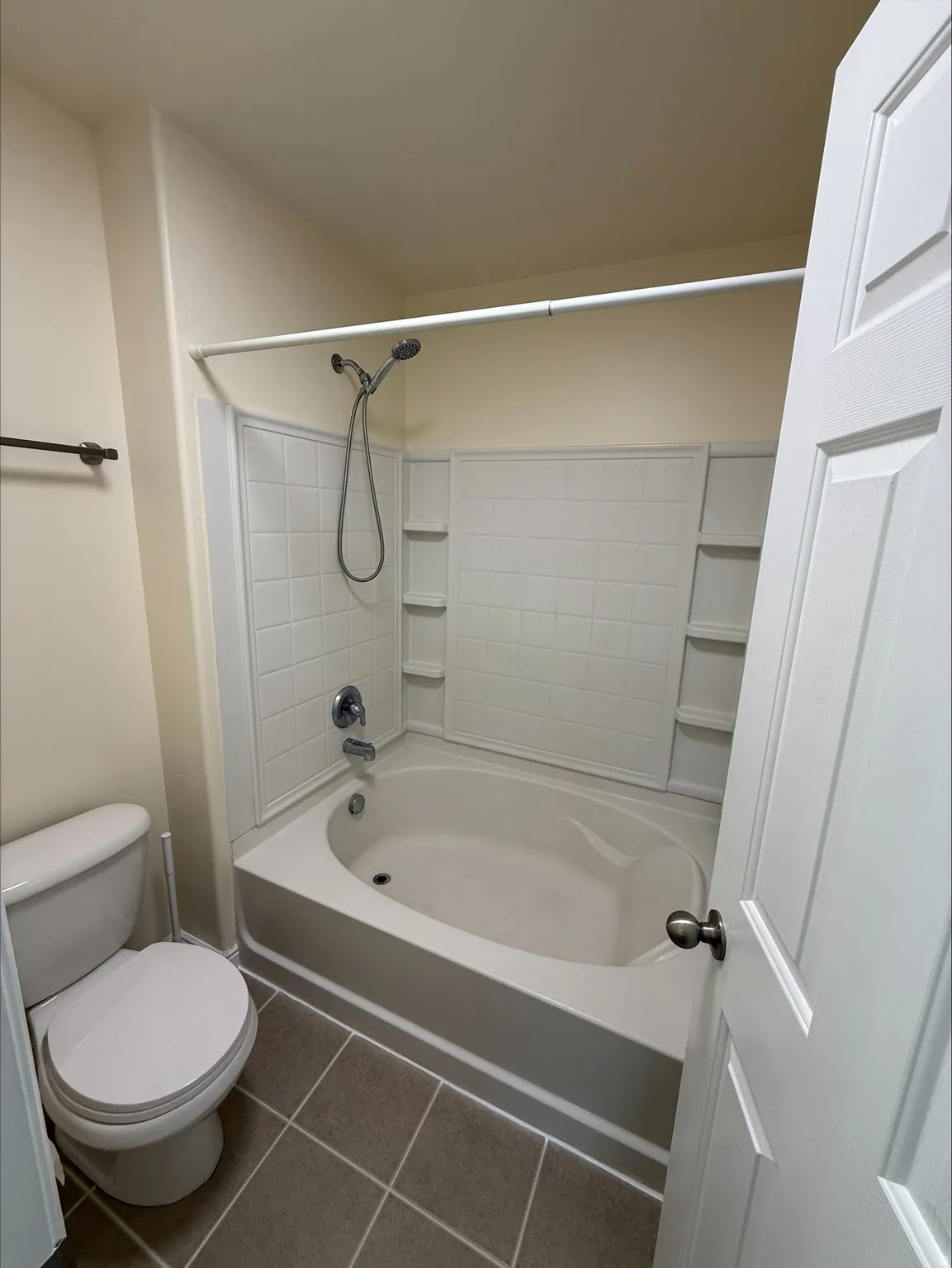 Tub and shower combination with a curved basin, integrated shelving, and a handheld showerhead