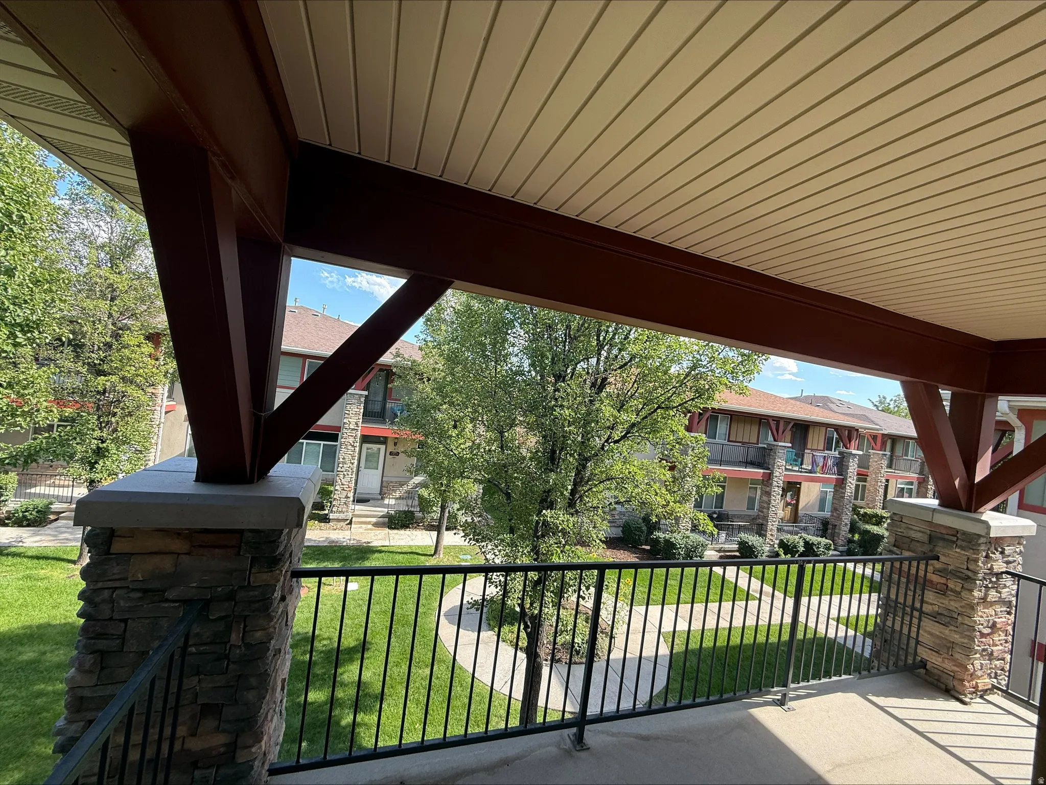 Covered balcony featuring stone-clad columns, dark wood-tone beams, and a slatted ceiling
