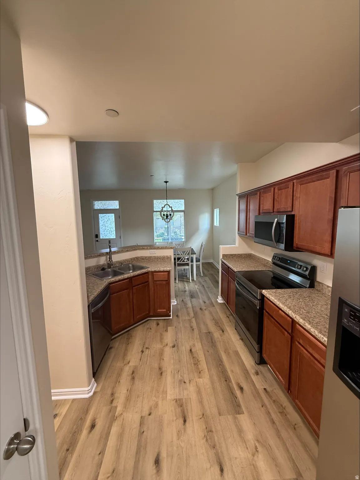 Kitchen featuring wood-finish flooring, wood cabinetry, granite-style countertops, stainless steel appliances, and a built-in double sink