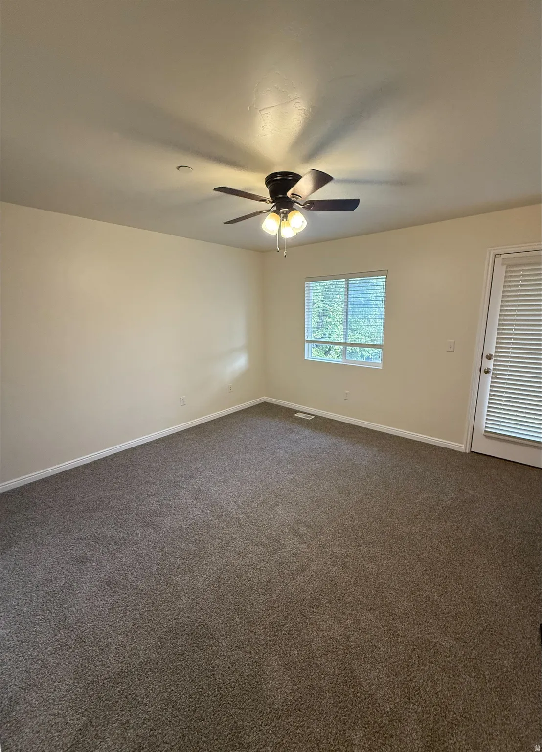 Spacious room featuring neutral carpet flooring, a ceiling fan with integrated lighting, and a white-framed window