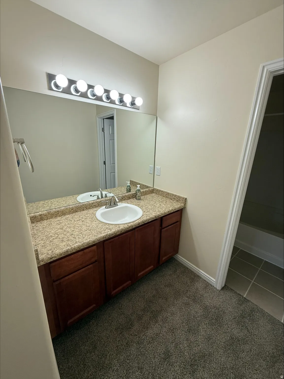 Vanity with a composite countertop and integrated sink, wood-finish cabinetry, and a multi-bulb light fixture