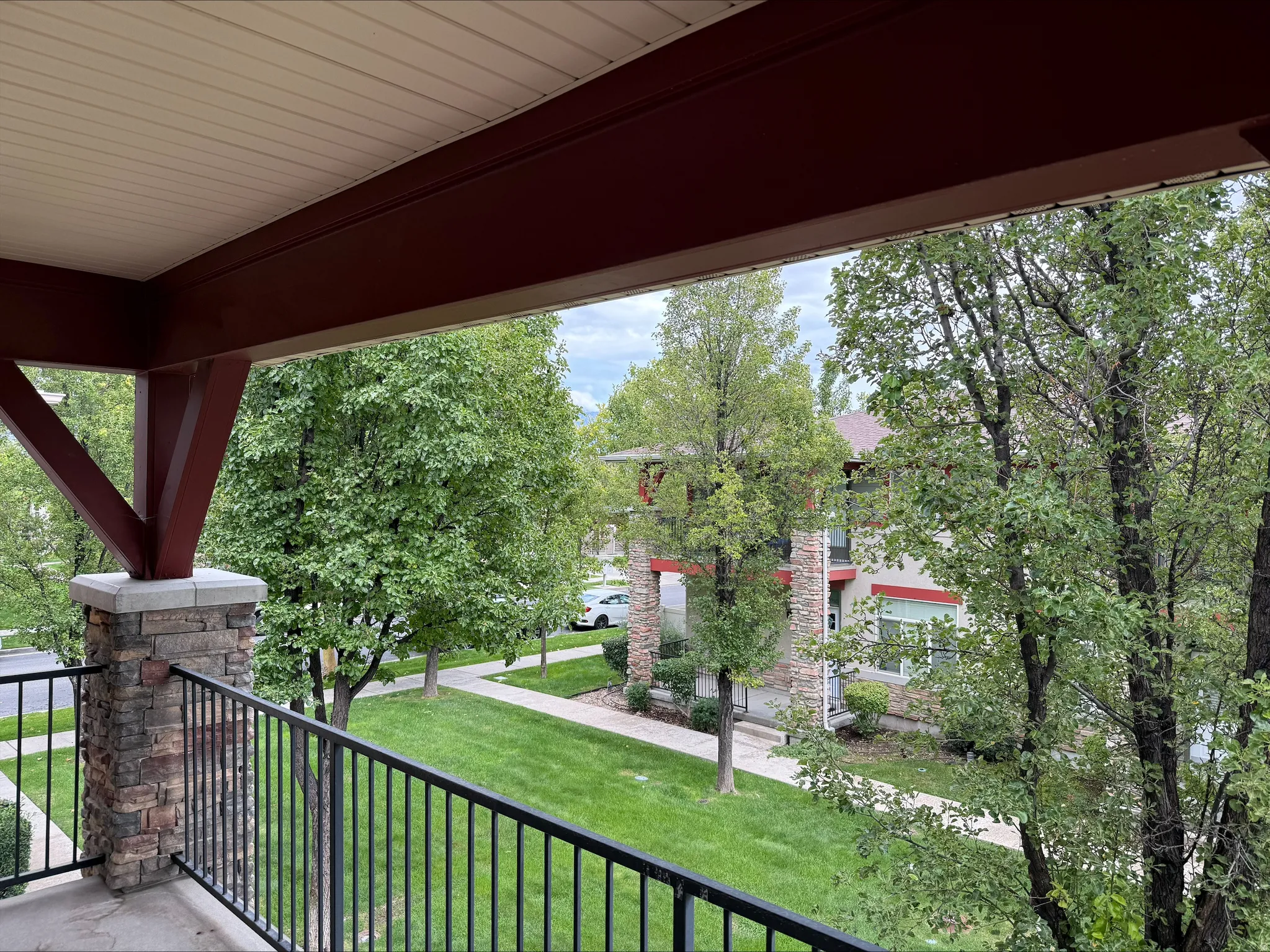 Stone-clad pillar with black metal railing, overlooking a green lawn with mature trees and paved walkway