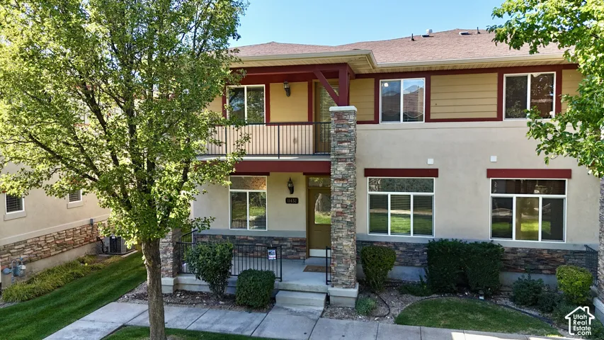 Two-story stucco and siding exterior with stone accents, a second-story balcony with metal railing, and multiple windows
