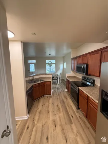 Kitchen featuring wood-finish flooring, wood cabinetry, granite-style countertops, stainless steel appliances, and a built-in double sink