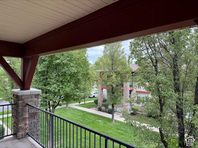 Stone-clad pillar with black metal railing, overlooking a green lawn with mature trees and paved walkway