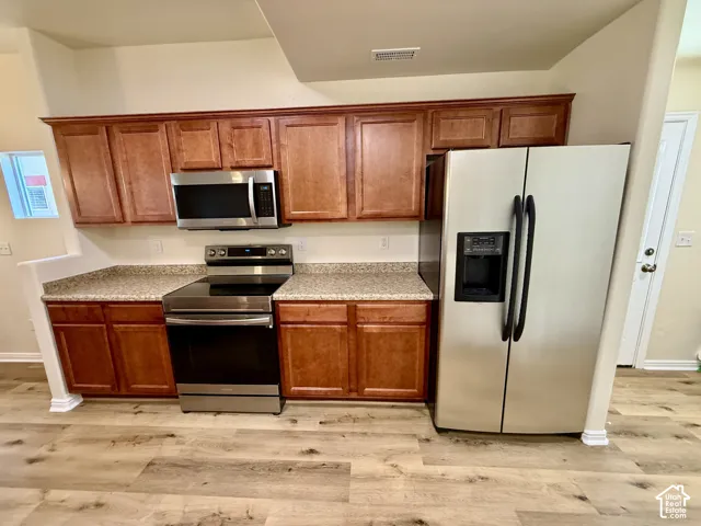 Kitchen with wood-finish flooring, stainless steel appliances, wood cabinetry, and speckled countertops