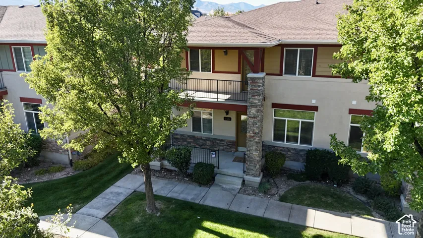 Multi-level exterior with a stone-clad column, second-story balcony with metal railing, and stucco siding