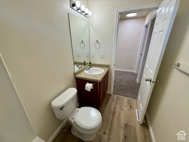 Wood-finish flooring, white toilet, vanity with integrated sink, granite-style countertop, and polished chrome light fixture