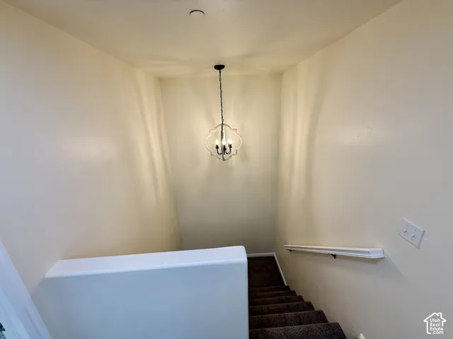 Stairwell featuring a decorative ceiling-mounted light fixture, neutral wall paint, white handrail, and carpeted stairs