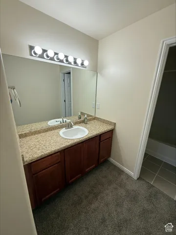 Vanity with a composite countertop and integrated sink, wood-finish cabinetry, and a multi-bulb light fixture