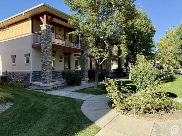Stucco and stone facade with an upper-level balcony, ground-level covered porch, and mature trees