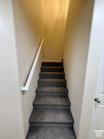 Carpeted staircase with light-toned walls and a white handrail