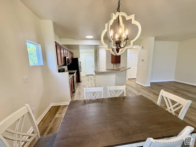 Open-concept living area with wood-finish flooring, a contemporary chandelier, and a kitchen featuring dark wood cabinetry, black appliances, and a breakfast bar with a stone-finish countertop