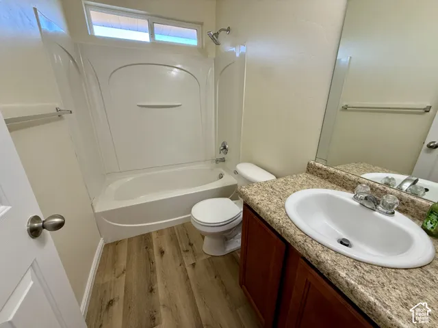 Bathroom featuring a white bathtub, white toilet, wood-finish flooring, and a vanity with a countertop and undermount sink