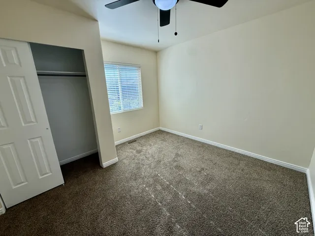 Carpeted room featuring a ceiling fan, window with blinds, and a built-in closet with sliding doors