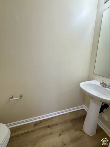 Pedestal sink with dual-handle faucet, wall-mounted mirror, wood-finish flooring, and white baseboard trim