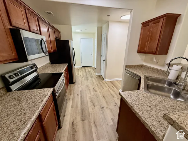 Kitchen featuring wood-finish flooring, stone-finish countertops, stainless steel appliances, and wood cabinetry