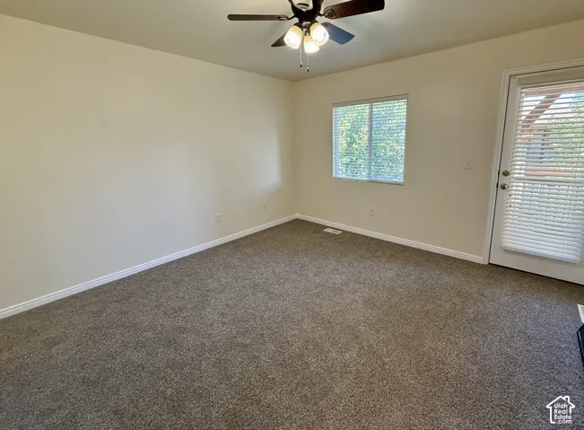 Neutral-toned carpeting, ceiling fan with integrated lighting, natural light from a window, and a door with an integrated blind