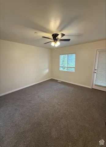 Spacious room featuring neutral carpet flooring, a ceiling fan with integrated lighting, and a white-framed window