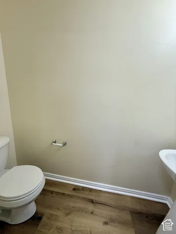 Wood-finish flooring with white trim, a toilet, and a wall-mounted toilet paper holder