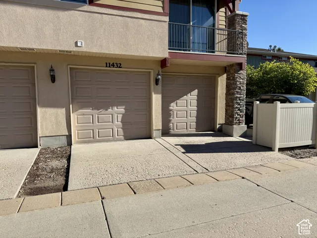 Stucco exterior with stacked stone accents, two paneled garage doors, and a second-story balcony with metal railing