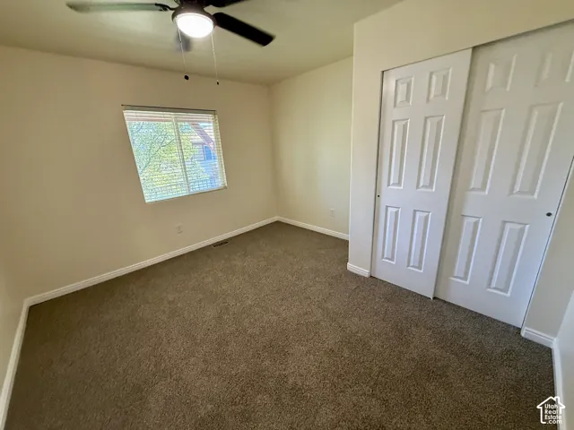 Carpeted room featuring a window with blinds, a ceiling fan with integrated lighting, and white sliding closet doors