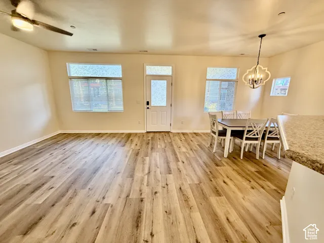 Spacious open-concept area featuring wood-finish flooring, a ceiling fan, a decorative chandelier, and multiple windows with blinds