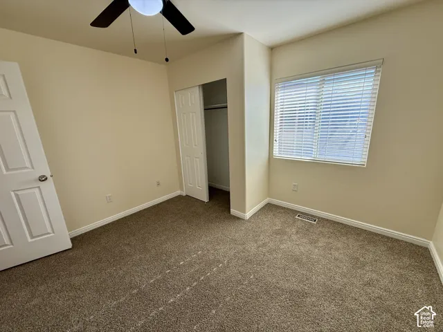 Room featuring carpet flooring, a ceiling fan with integrated lighting, a window with blinds, and a built-in closet with bi-fold doors