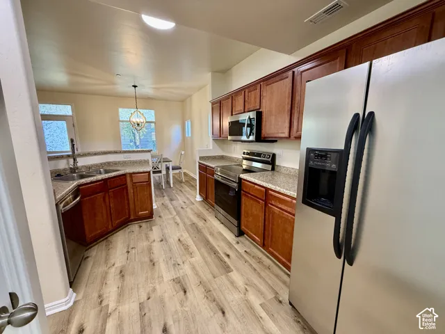 Kitchen featuring wood-finish flooring, stainless steel appliances, wood cabinetry, stone-look countertops, and recessed lighting
