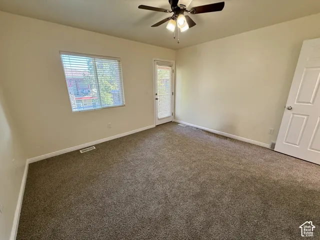 Carpeted room featuring a ceiling fan with integrated lighting, a window with horizontal blinds, and a glass-paneled door