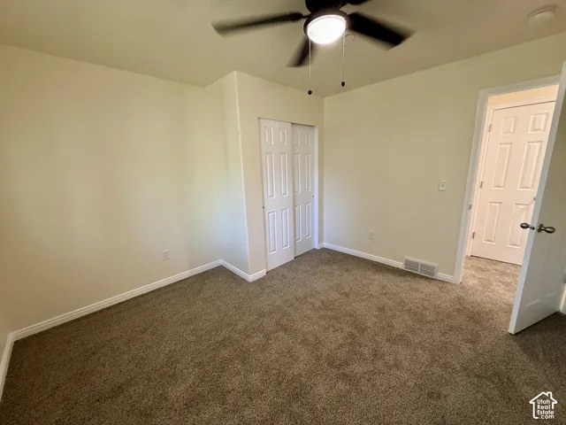Neutral tone wall paint, brown carpet flooring, ceiling fan with integrated lighting, bi-fold closet doors, and white trim throughout