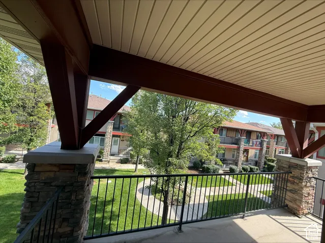 Covered balcony featuring stone-clad columns, dark wood-tone beams, and a slatted ceiling